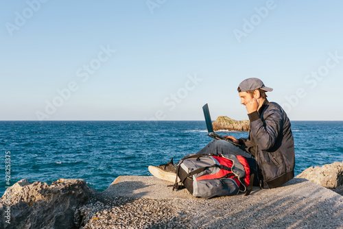 digital nomad working with his computer during a trip. person celebrating a triumph and looking at her laptop in front of the coast. working remotely.