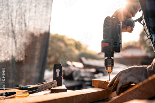 A carpenter using a drilling tool or an electric screwdriver is working at home on the wooden floor. Ideas for home improvement and extension.