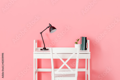 Modern workplace with lamp on color background