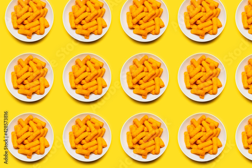 Pattern of white bowls with corn puffs on yellow background.