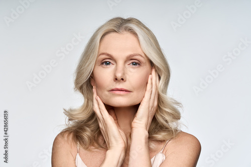 Adult senior older woman touching her perfect skin. Beautiful portrait mid 50s aged woman advertising facial anti age lift products salon care tighten skin isolated on white looking at camera.