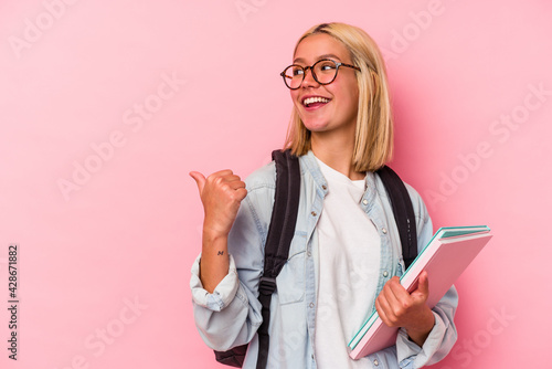 Young venezuelan student woman isolated on pink background points with thumb finger away, laughing and carefree.