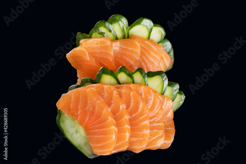 salmon sashimi and slices of cucumber on black background