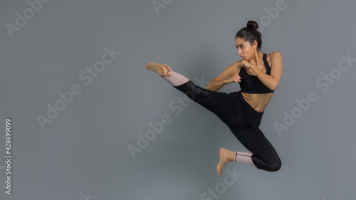 Joven mujer latina mexicana atleta entrenando artes marciales: taekwondo, karate, box. Vestida de negro y haciendo ejercicio con fondo gris