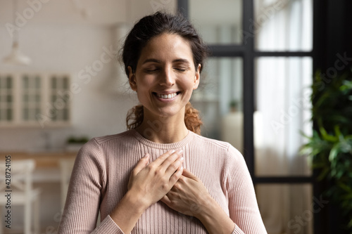 Thank you my God. Happy peaceful millennial hispanic lady stand alone with closed eyes keep hands close to heart hope pray in mind. Emotional young woman express deep gratitude impressed by good deed