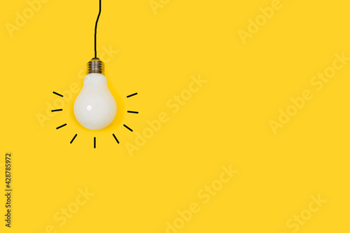 Bombilla de luz colgante sobre un fondo amarillo liso y aislado. Vista de frente y de cerca. Copy space