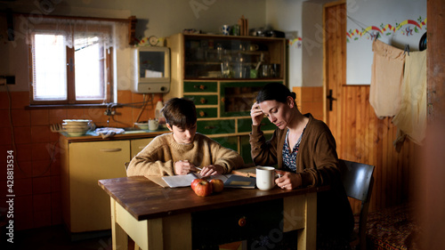 Poor mature mother and small daughter learning indoors at home, poverty concept.