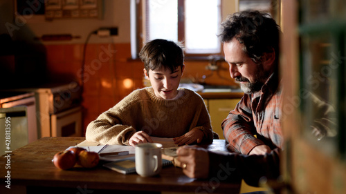 Poor mature father and small daughter learning indoors at home, poverty concept.