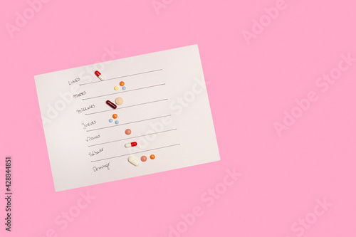 Vitaminas y suplementos multicolores sobre un fondo de papel de calendario sobre un fondo rosa liso y aislado. Vista superior. Copy space