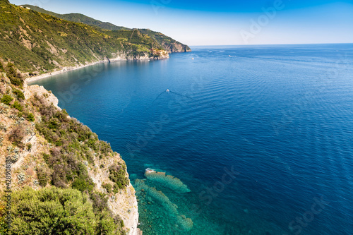 Corniglia, Liguria, Italy. June 2021. Amazing maritime landscape of the Cinque Terre: crystal clear sea, luxuriant nature. In the background the small village of Manarola.