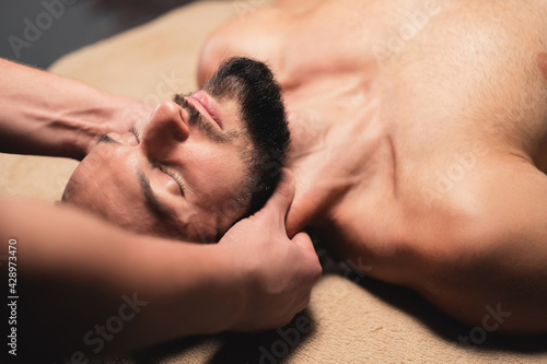 In a professional massage parlor, a Caucasian male athlete with a beard is kneading the neck. Sports massage of the lateral longitudinal muscles of the neck