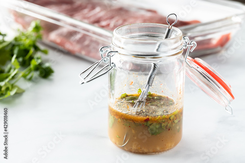 Close up of a small jar filled with a cilantro lime marinade mixture with raw flank beef in behind.