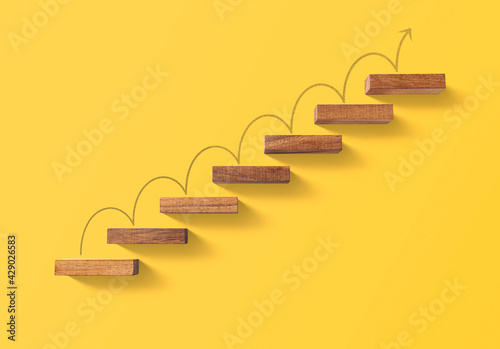 Step by step to grow your business, business success or career path success concept. Wooden blocks arranged in a shape of staircase on yellow background.