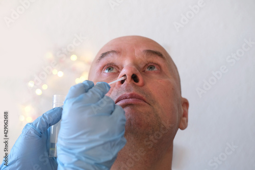 face of an elderly bald man close-up, laboratory assistant, doctor takes swab sample from the nasal mucosa for test for coronavirus, DNA determination, concept of COVID-19