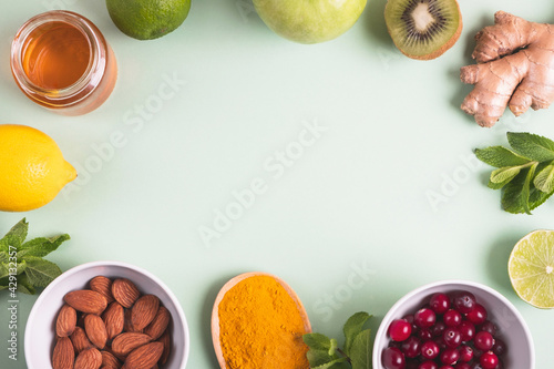 Healthy products for immunity boosting on green background. Fruits, honey, berries, ginger root, mint, nuts and turmeric. Health, virus prevention. Top view, flat lay, copy space, frame