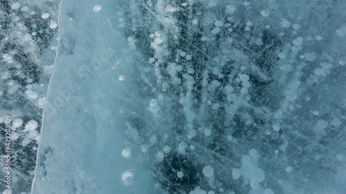Ice, close-up, details. Cracks are visible on the transparent shiny surface. Columns of frozen methane gas bubbles go into the depths. Lake Baikal