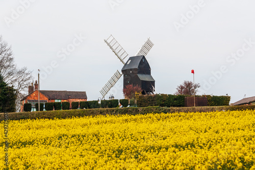 Dale Abbey, Ilkeston, UK, April,18,2021: The cat and fiddle windmill in the rural landscape in spring time pictured with a field of rapeseed plant.