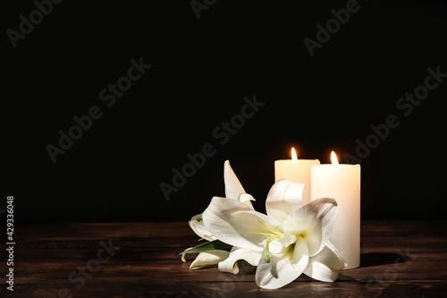Candles with lily flowers on table against dark background