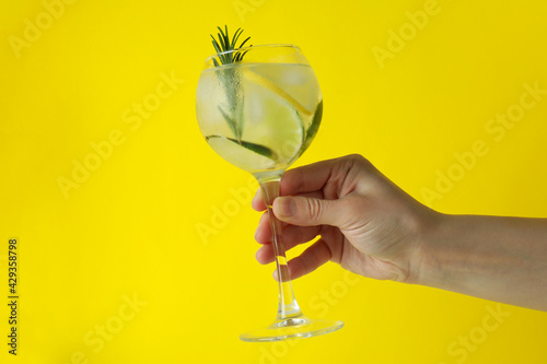 Female hand hold glass of cocktail with citrus and rosemary on yellow background