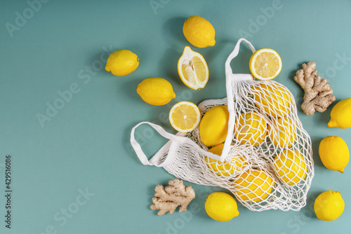 Healthy products in the form of lemons and ginger roots on string bag, on simple light green background with copy space, the concept of eco-friendly and healthy lifestyle.