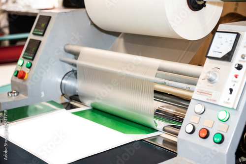 The industrial laminator applies the film to the paper in the production room of the printing house