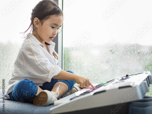 Portrait asian girl child look adorable and very cute playing music electronic keyboard feel casual and relaxation in home.