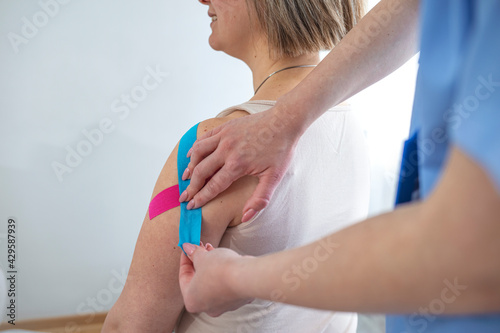 Kinesiology taping. Physical therapist applying kinesiology tape to patient neck. Therapist treating injured trapezius muscles of young athlete. Post traumatic rehabilitation, sport physical therapy.