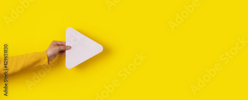 hand holding media player button icon over trendy yellow background, panoramic layout