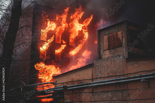 Massive large blaze fire in the city, brick factory building on fire, hell major fire explosion flame blast, with firefighters team firemen on duty, arson, burning house damage destruction