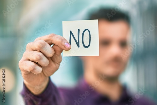 Young hispanic man with serious expression holding no reminder paper at the city.