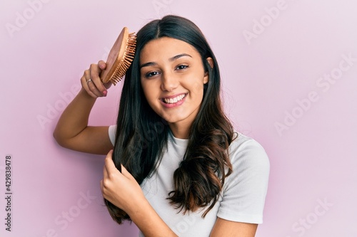 Young hispanic woman styling hair using comb smiling with a happy and cool smile on face. showing teeth.