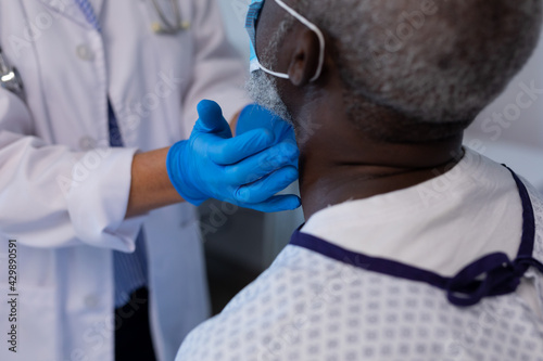 Caucasian female doctor palpating lymph nodes of african american male patient wearing mask