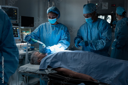 Diverse surgeons with face masks and protective clothing during operation, sedating patient