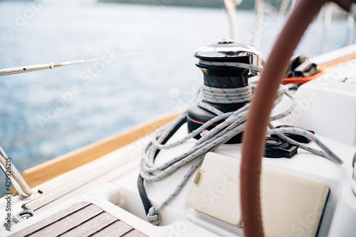 Black halyard winch with a white cable coiled around against the background of the bow of sailboat
