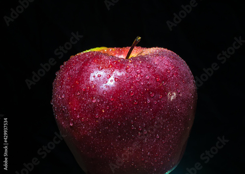 głęboko czerwone jabłko pokryte kroplami wody na czarnym tle