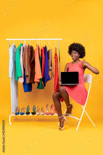 Black Shopaholic Woman Showing Laptop Screen Gesturing Thumbs-Up, Yellow Background