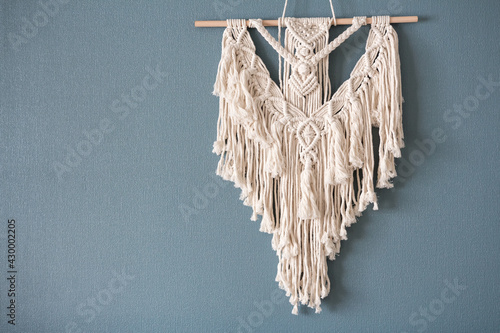 Macrame. Handmade macrame weaving and cotton threads on a rustic wooden stick. Scandinavian style in the interior, boho style. Cozy home