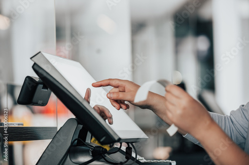 Young saleswoman doing process payment on touchscreen POS, counting sale in the cash register, finance concept