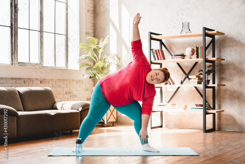 Plus size corpulent young woman doing physical exercises indoors for being in good shape. Dieting and healthy lifestyle for burning fat and calories