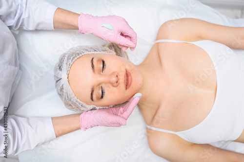 Beautiful happy woman receiving spa treatment. Cosmetologist in beauty salon with a pink glove applies a moisturizing cream mask. Facial beauty. Perfect fresh clean skin. Youth and skin care concept 