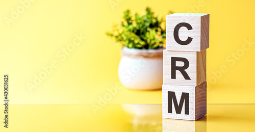 Three wooden cubes with letters - crm - Customer Relationship Management, on blue table, space for text in left. Front view concepts, flower in the background.