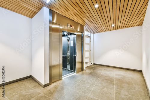 Shiny elevator with opened door located in illuminated hall of contemporary apartment building with tiled floor