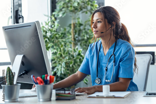 Female doctor talking with earphone while explaining medical treatment to patient through a video call with computer in the consultation.