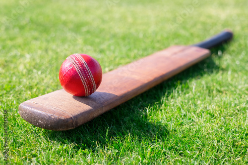 Cricket ball on top of cricket bat on green grass of cricket pitch