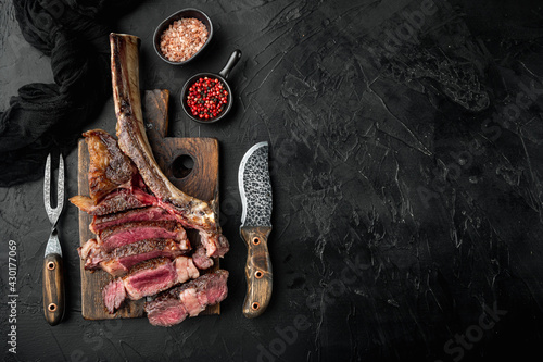 Sliced barbecued tomahawk rib tip with rosemary, salt and herbs medium rare, on wooden serving board, on black stone background, top view flat lay, with copy space for text