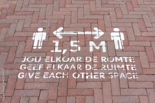 Social distancing sign painted on the street to advise pedestrians to keep 1,5 meters apart during the coronavirus covid-19 pandemic. Sign with text in the frisian, dutch and english language. 