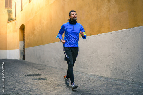 Male running and listening music during workout. Man run in the city and jogging alone. Runner with mobile phone connected to a smart watch recording data of sport activity with wearable technology.