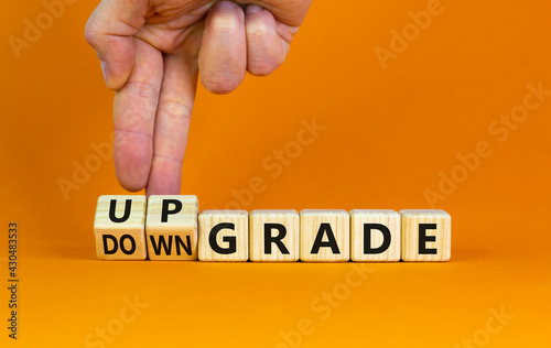 Upgrade or downgrade symbol. Businessman turns wooden cubes, changes words 'downgrade' to 'upgrade'. Beautiful orange table, orange background, copy space. Business and upgrade or downgrade concept.