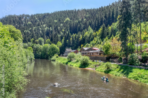 Panoramic view of the Svatos Rocks National Park (Czech Republic) on a sunny spring day. There are many green plants on the banks. Rafting down the Ohře river. Tourists rest in the distance 