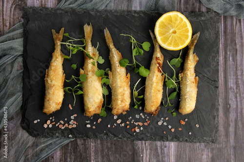 fried breaded fish served on a black stone, decorated with fresh lemon, dark wooden background. horizontal view from above 